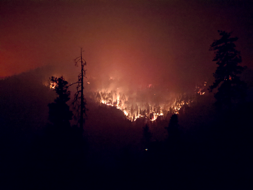 dark foreground, valley of trees on fire glow in distance.